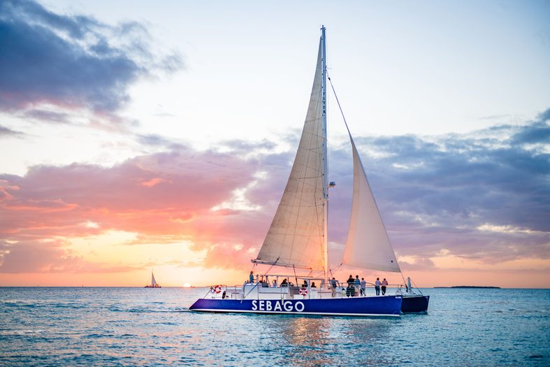 Blue Catamaran at sunset with a few people on board