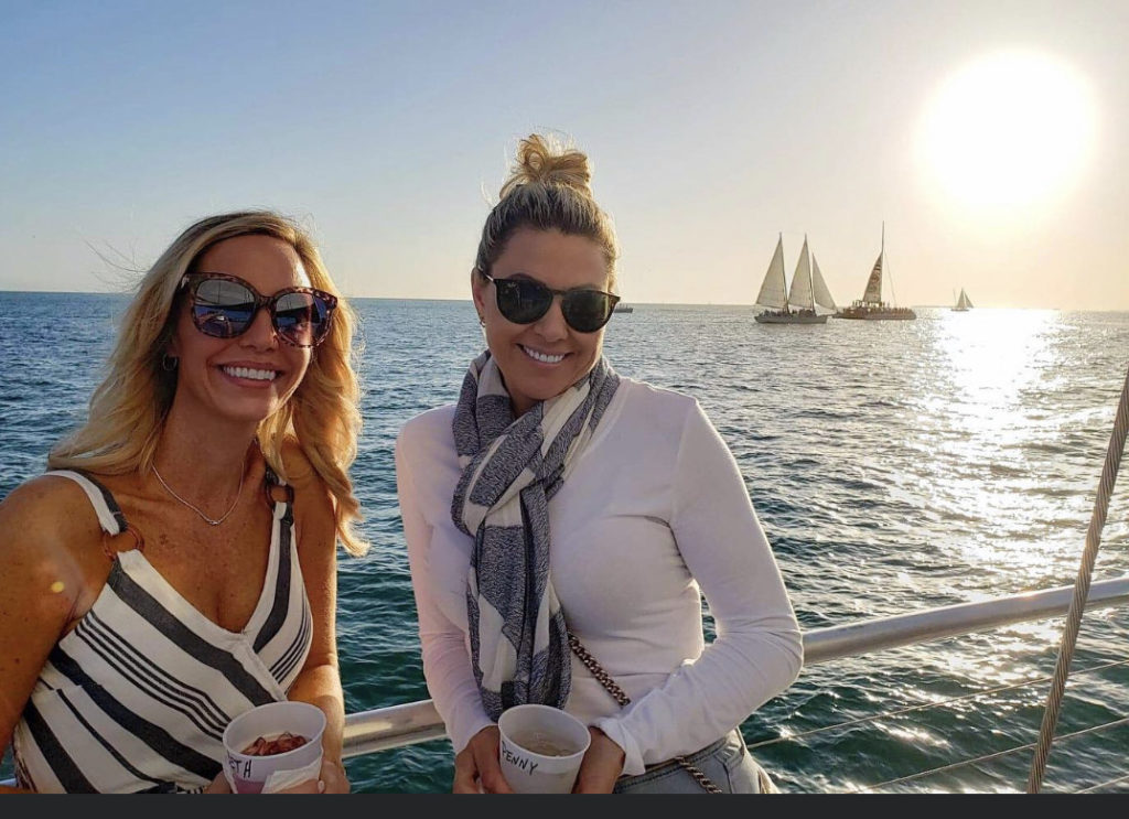 two women enjoying a boat ride with sunset in the background